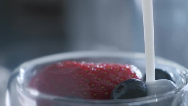 Giet natuurlijke biologische melk of yoghurt in een keramische kom met een gezonde mix van verse biologische vruchten en bessen.  - Video