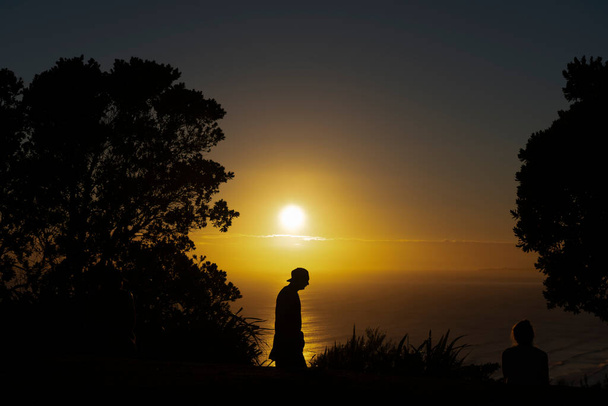 Maunganui Dağı 'nın zirvesinden altın güneşe bakın. Sabahın erken saatlerinde insanlar egzersiz yapmak için arka planda ve siluette tanınmaz haldeler. - Fotoğraf, Görsel
