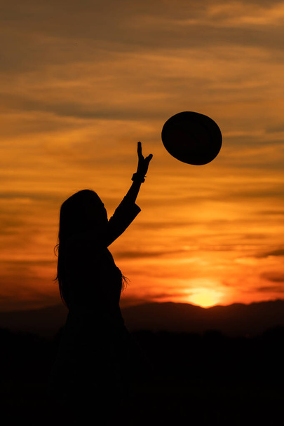 silhouet van meisje gooien een hoed in de lucht tijdens een gouden zonsondergang - Foto, afbeelding