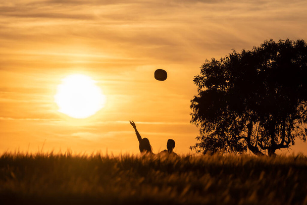 silhueta de menina e menino jogando chapéus no ar em um pôr do sol no campo com o pôr do sol no fundo - Foto, Imagem