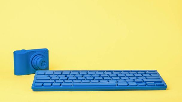 Ένα φωτεινό μπλε πληκτρολόγιο και μια φωτεινή μπλε κάμερα σε κίτρινο φόντο. Κομψά αξεσουάρ για επιχειρήσεις και freelancing. - Φωτογραφία, εικόνα