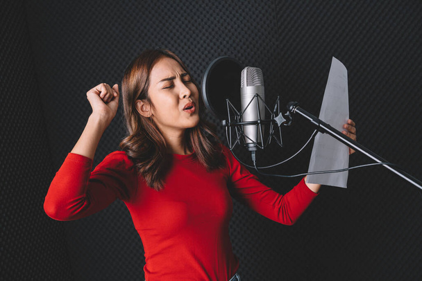 Csinos ázsiai énekesnő dalokat rögzít stúdió mikrofonnal és pop pajzzsal mikrofonon, szenvedéllyel a zenei stúdióban. Előadás és show a zeneiparban. Fénymásolós kép. - Fotó, kép