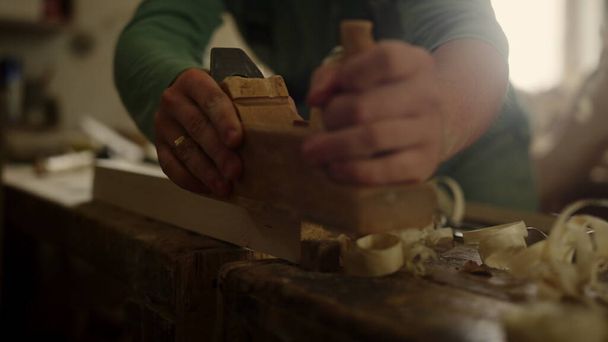 Άγνωστος ξυλουργός χρησιμοποιεί αεροπλάνο στο εργαστήριο. Χειροτεχνίας χέρια προετοιμασία σανίδα  - Φωτογραφία, εικόνα