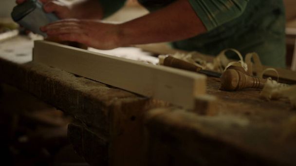 Ο άνθρωπος ελέγχει την απαλότητα του ξύλου στο στούντιο. Άγνωστος τύπος που χρησιμοποιεί γυαλόχαρτο στην ξυλουργική  - Φωτογραφία, εικόνα