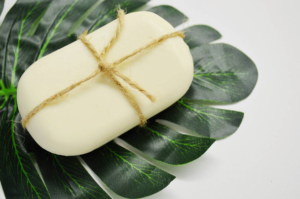 Λευκό σαπούνι δεμένο με σχοινί βρίσκεται σε ένα πράσινο φύλλο φοίνικα σε λευκό φόντο - Φωτογραφία, εικόνα