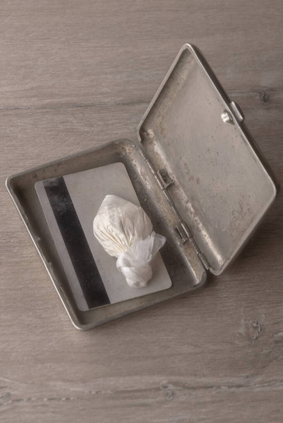 dose de cocaïne dans un sac en plastique et une carte à l'intérieur d'un étui à cigarettes ouvert, sur fond sombre, contraste réduit - Photo, image
