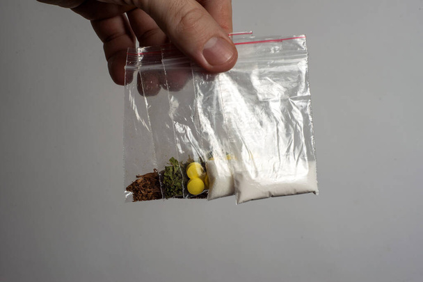 dodencel concept: tabak, wiet, MDMA tabletten, amfetamine kristallen, heroïne in plastic zakken, op een lichte achtergrond. Verbeterd contrast, gedeeltelijke vervaging. - Foto, afbeelding