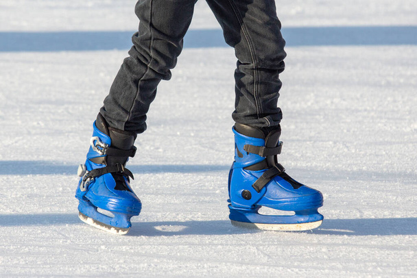 Τα πόδια ενός άντρα με μπλε πατίνια οδηγούν σε παγοδρόμιο. χόμπι και αναψυχή. χειμερινά αθλήματα - Φωτογραφία, εικόνα