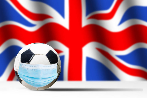 Fußball in medizinischer Maske vor dem Hintergrund der britischen Flagge. Coronaschutz gegen Viren Bakterien stoppen. Absage von Sportveranstaltungen. Kopierraum - Foto, Bild