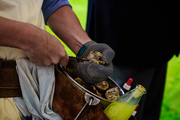 close-up van de hand van een man met een ketting handschoen gooien een oester - Foto, afbeelding