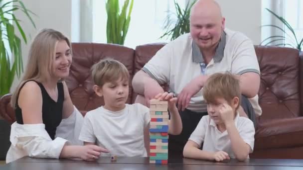 Famiglia spensierata di due figli che giocano nel gioco da tavolo, torre di legno in soggiorno - Filmati, video