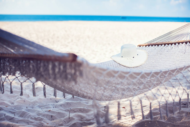Λευκό καπέλο στην αιώρα στην τροπική παραλία άμμο για φόντο το καλοκαίρι - Φωτογραφία, εικόνα