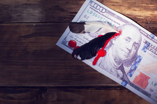 Ένα χαρτονόμισμα των 100 δολαρίων με φτερό στο κεφάλι του προέδρου και αίμα από κοντά. Έννοια πολέμου κόκκινου δέρματος - Φωτογραφία, εικόνα