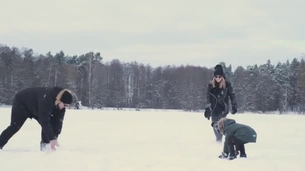 Familia feliz con un niño jugando bolas de nieve en invierno en el bosque en el río - Metraje, vídeo