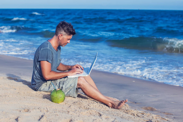 Fiatal férfi ül a strandon laptoppal - Fotó, kép