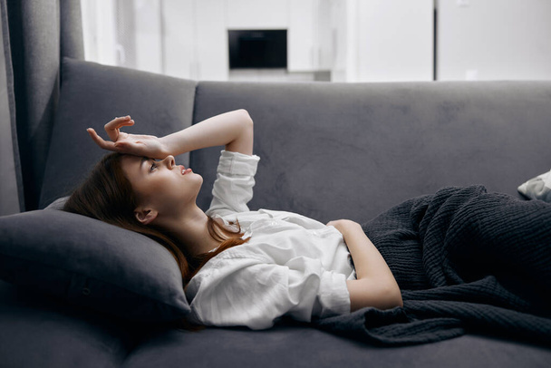 Nainen pitää kättään päänsä päällä makaa sohvalla tunne huonovointisuus - Valokuva, kuva