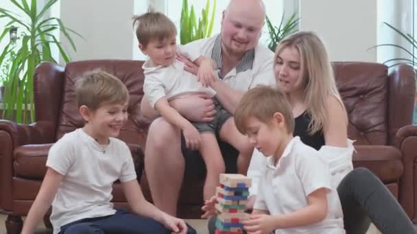 Vriendelijke familie spelen houten toren en juichen elkaar, vallende toren - Video