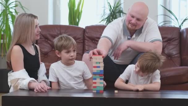 Ευτυχισμένη οικογένεια τεσσάρων ατόμων που παίζουν σε επιτραπέζιο παιχνίδι, ξύλινο πύργο - Πλάνα, βίντεο