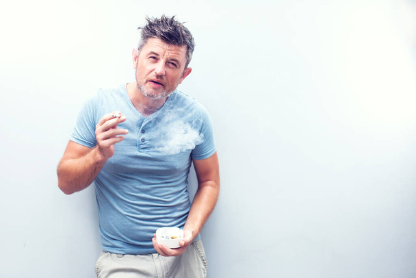 Hezký mladý muž s hnědými vlasy v košili izolované na šedém pozadí. Kouřící cigareta. - Fotografie, Obrázek