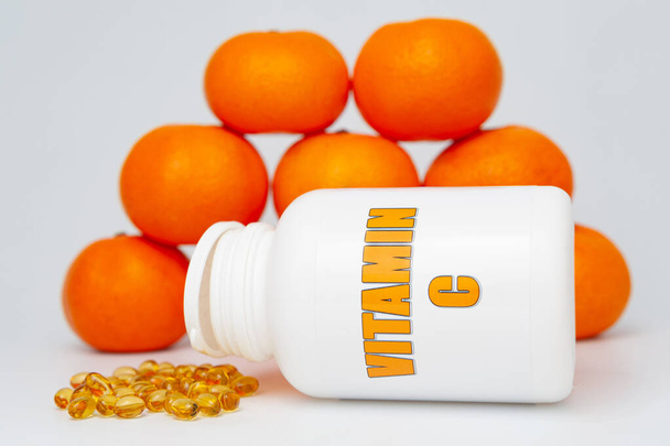 Frasco de vitamina C con gel blando y naranjas dispersas. Aislado sobre fondo blanco. Sistema inmunitario sano. - Foto, imagen