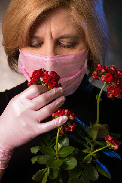 El hombre huele una flor interior de Kalanchoe con capullos rojos. Utiliza medidas de protección contra el virus. El síntoma es la falta de olfato. Violación de las funciones cognitivas del cuerpo humano. Catástrofe mundial. - Foto, Imagen