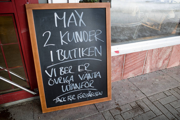 スウェーデン・ストックホルムホグダレン郊外の魚屋の前でスウェーデンの看板には、「店内で最大2人の顧客がいます。他は外で待ってください." - 写真・画像