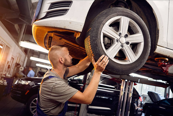 Handsome auto mechanic installs and inspects the wheels on the car. Torsion of wheels on service station  - Photo, Image