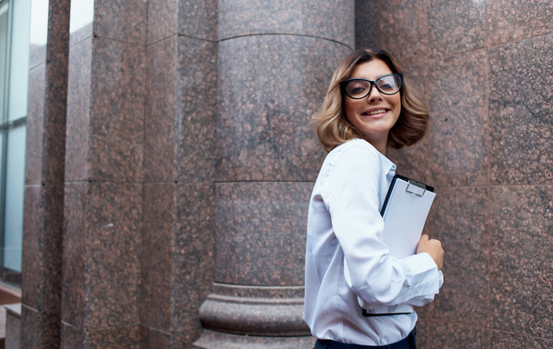 счастливая деловая женщина возле здания с документами в руках и очками на лице обрезанный вид - Фото, изображение