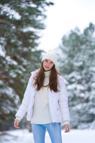 красивая улыбающаяся молодая женщина в зимнее время на открытом воздухе. Зимняя концепция. белая одежда, снег, лес, холодная погода, замороженные - Фото, изображение