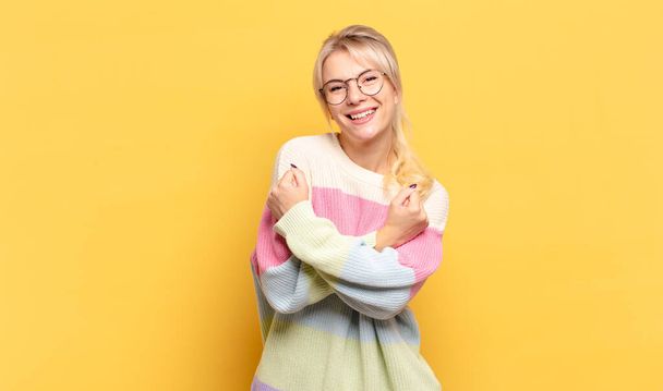 blonde woman smiling cheerfully and celebrating, with fists clenched and arms crossed, feeling happy and positive - 写真・画像