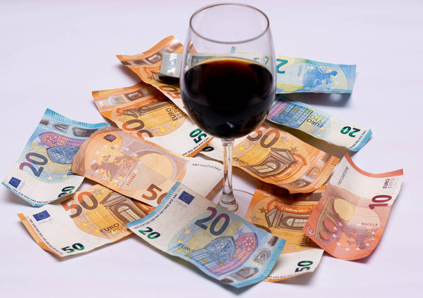 glas wijn met veel geld op de vloer, eurobiljetten van vijf, vijftig, twintig en tien. - Foto, afbeelding