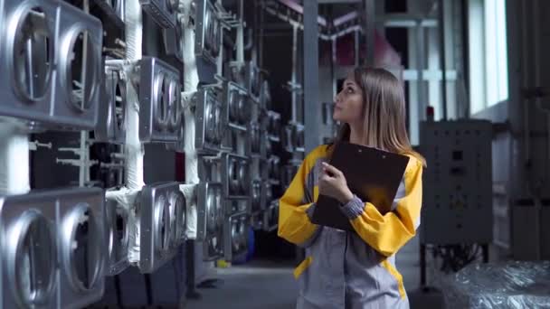 Egy fiatal, csinos, fehér nő dolgozik a gyár festőműhelyében, ellenőrzi a festetlen fémtermékeket, és feljegyzéseket készít az ellenőrzőlistában.. - Felvétel, videó