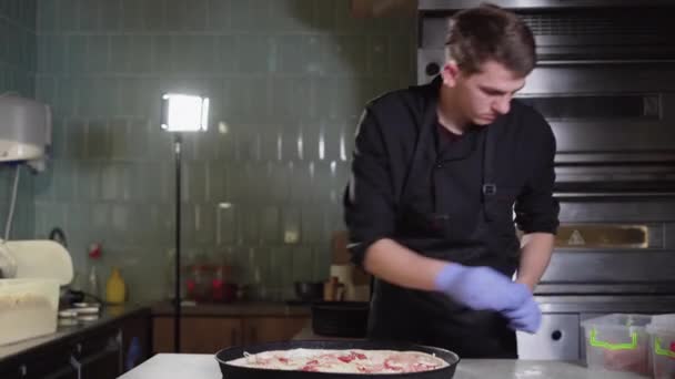 chef with gloves puts ham or meat on pizza, prepares pizza in a restaurant. - Záběry, video