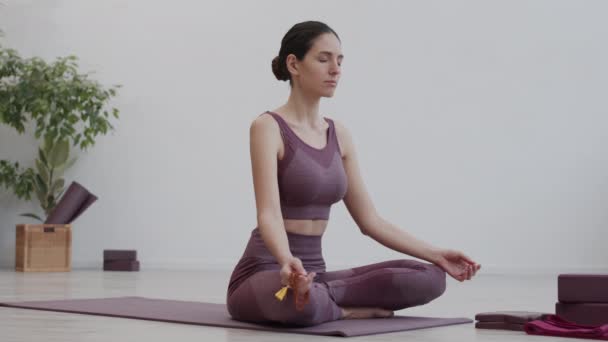 Ampla foto da jovem esportista caucasiana segurando contas mala enquanto meditava na posição de lótus no estúdio de ioga - Filmagem, Vídeo