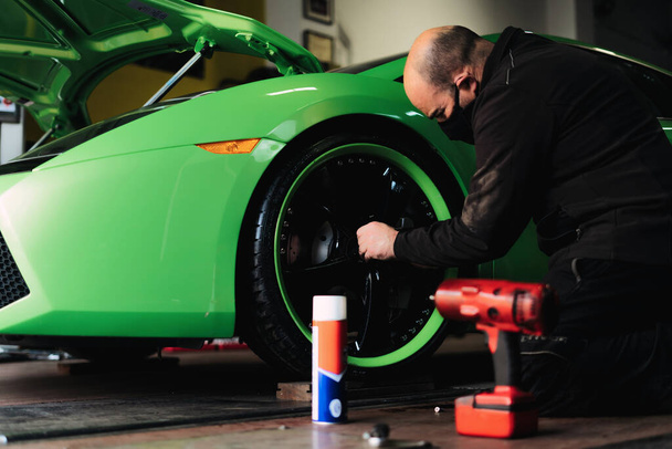Tamirci üst düzey bir süper spor arabanın tekerlerini değiştiriyor. Otomobil tamircisi garajda çalışıyor. Onarım servisi. - Fotoğraf, Görsel
