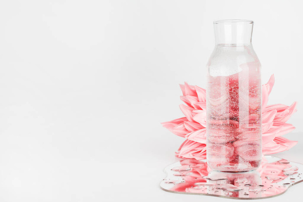 рожеві квіти, спотворені через воду в пляшці з дзеркалом на білому тлі. чиста вода, екологічно чиста домашня концепція
.  - Фото, зображення