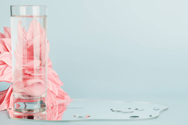 Rosafarbene Blumen, die durch Wasser in Glas mit Spiegel auf blauem Hintergrund verzerrt wurden. reines Wasser, entspannen, surreales Konzept - Foto, Bild