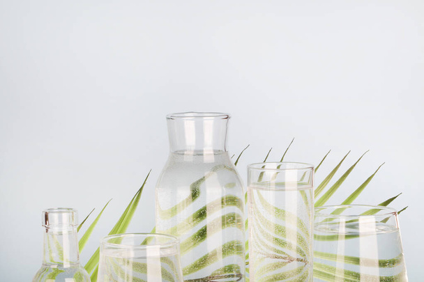 Palmblatt verzerrt durch Wasser in Gläsern und Flaschen auf blauem Hintergrund. Wohnkultur, Gartenkonzept - Foto, Bild