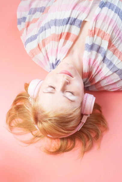 Chica caucásica en una sudadera rosa y con auriculares de color rosa sobre un fondo similar en tono. Concepto de música, podcasts, audiolibros. Día Mundial de la Música, Día Mundial del Rock-n-roll. - Foto, Imagen