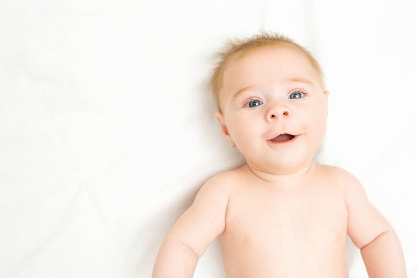 大きな笑顔で幸せな新生児の男の子。可愛い赤ん坊は白い背景に横たわって、スペースをコピーします。面白いです子供赤い目と生姜髪見ますカメラ - 写真・画像