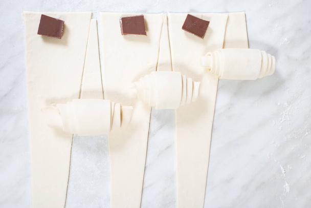 Hacer croissants con chocolate, en una mesa de cocina blanca. - Foto, Imagen