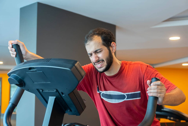 Arabischer Mann trainiert mit Crossmaschine, um seine Ausdauer im Fitnessstudio zu steigern - Foto, Bild