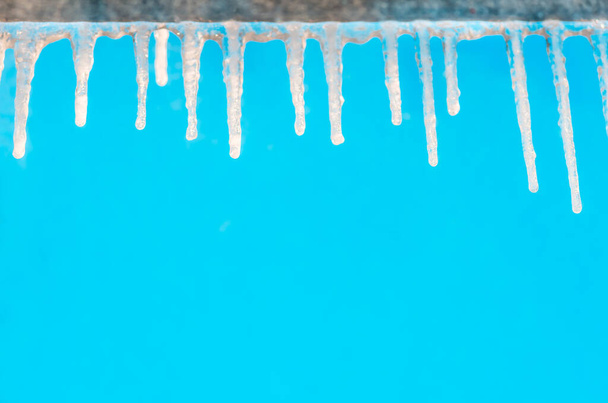 Gefrorene Eiszapfen hängen an einem klaren Tag an einem Gesims vor blauem Himmel - Foto, Bild