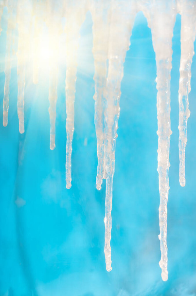 Bevroren ijspegels hangen op een heldere dag op een blauwe achtergrond - Foto, afbeelding