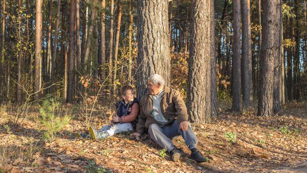 Szczęśliwe dziecko z dziadkiem bawiącym się w lesie. Dziadek na emeryturze. Emerytowany rodzic. Portret zamyślonego starszego pana i jego wnuka. Starszy mężczyzna zabawia się ze swoim wnukiem na świeżym powietrzu. - Zdjęcie, obraz