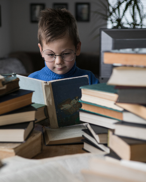 Niño de cinco años con gafas leyendo un libro con un montón de libros a su lado. Niño inteligente inteligente preescolar elegir libros para pedir prestado. - Foto, Imagen