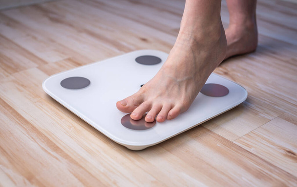 女性の裸の足は木製の床の上の電子スケールに立つ。フィットネスと減量の追跡の概念 - 写真・画像