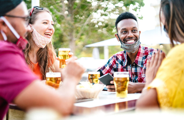 Pessoas multiculturais bebendo cerveja com máscaras abertas - Novo conceito de reunião normal com amigos se divertindo juntos na happy hour no bar cervejaria - Filtro brilhante com foco no cara afroamericano - Foto, Imagem