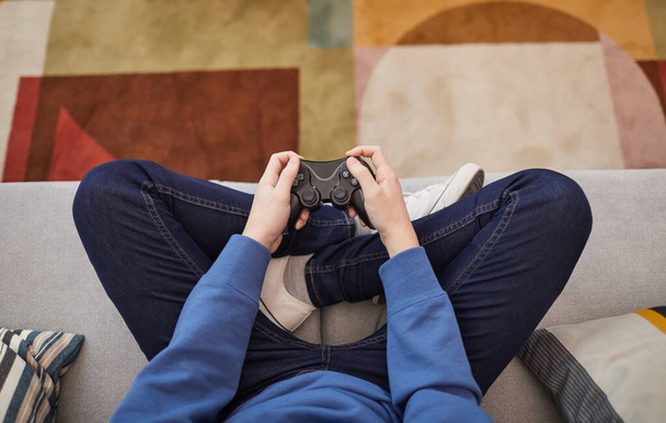 Visão de cima para baixo em menino adolescente irreconhecível jogando videogames enquanto sentado no sofá e segurando gamepad, espaço de cópia - Foto, Imagem