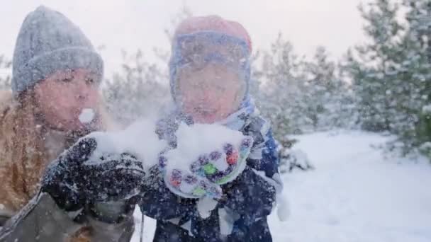 Bella allegra mamma e figlio tenendo la neve in mano e soffiando fuori sulla macchina fotografica, facendo piccola tempesta di neve, divertirsi, godendo passatempo nella foresta innevata, momenti invernali, rallentatore - Filmati, video
